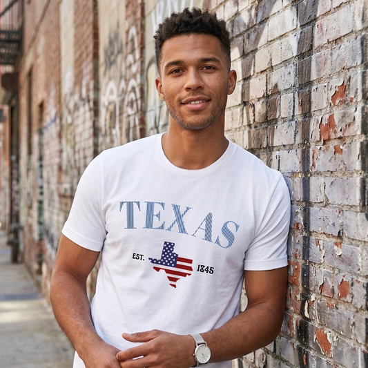 Man wearing a white t-shirt with 'TEXAS' design leaning against a brick wall.