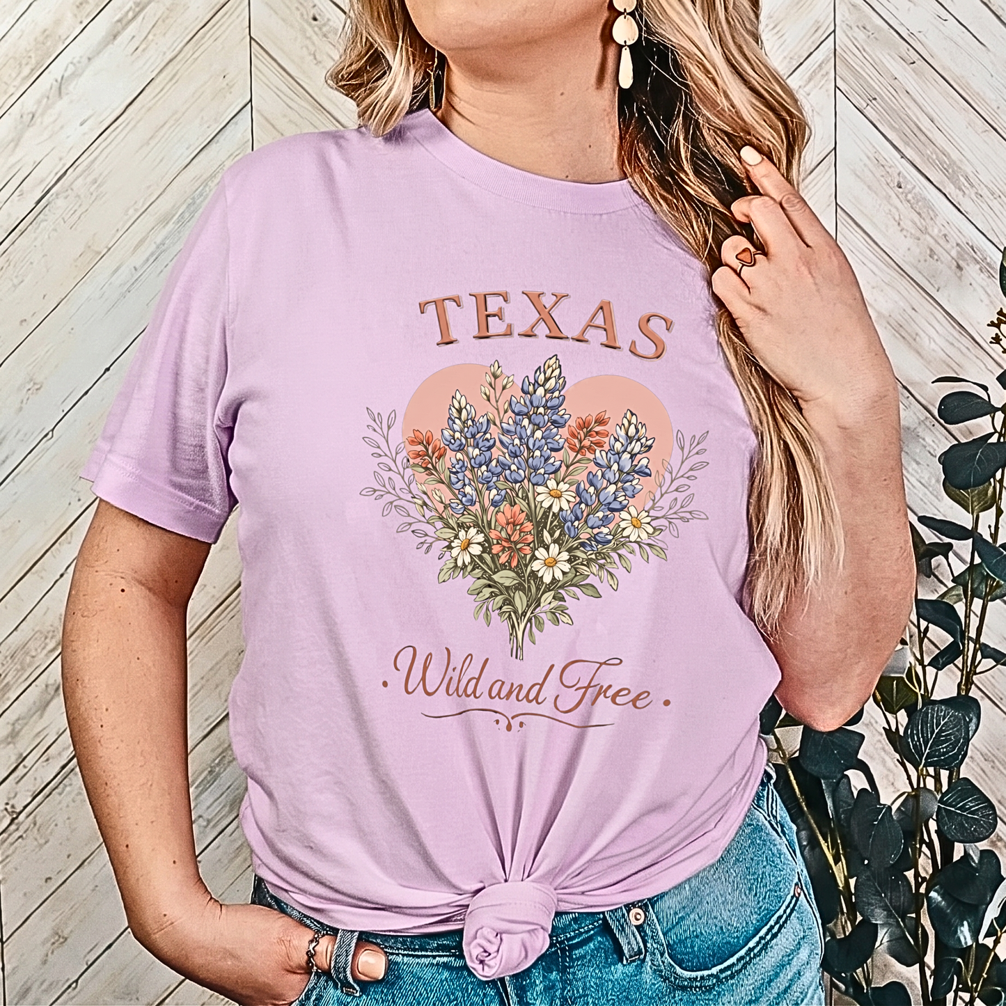 Person wearing a lavender t-shirt with 'Texas Wild and Free' design against a wooden wall.