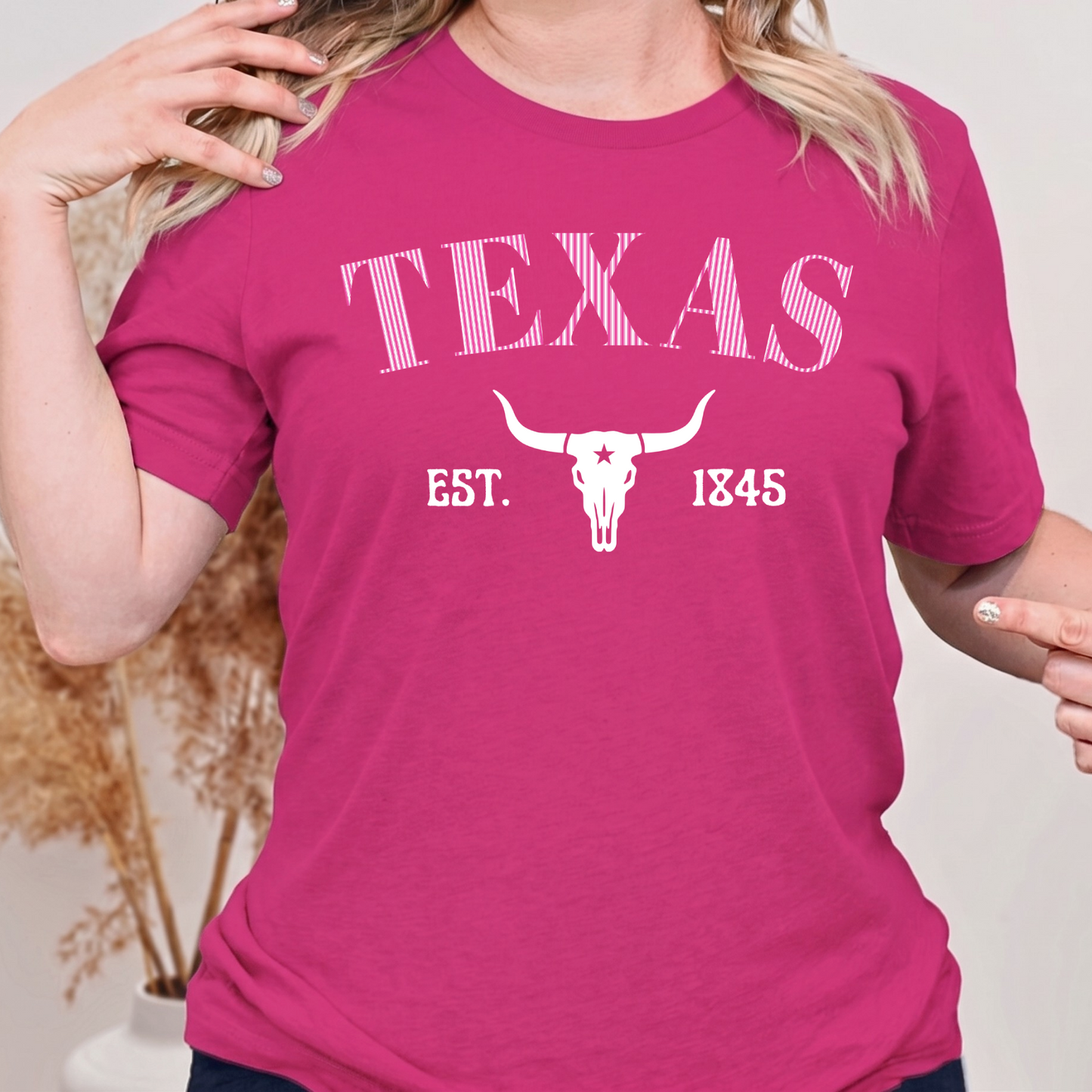 Person wearing a bright berry pink t-shirt with 'Texas Est. 1845' design