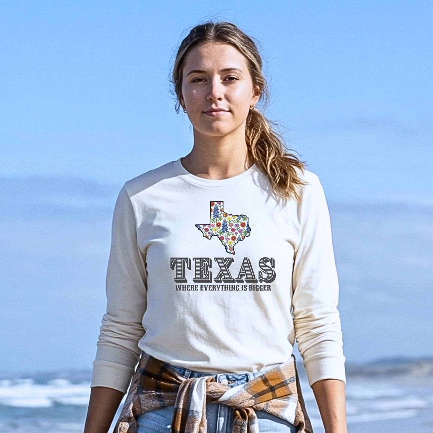 Woman wearing a white sweatshirt with 'Texas' and a map design on a beach.