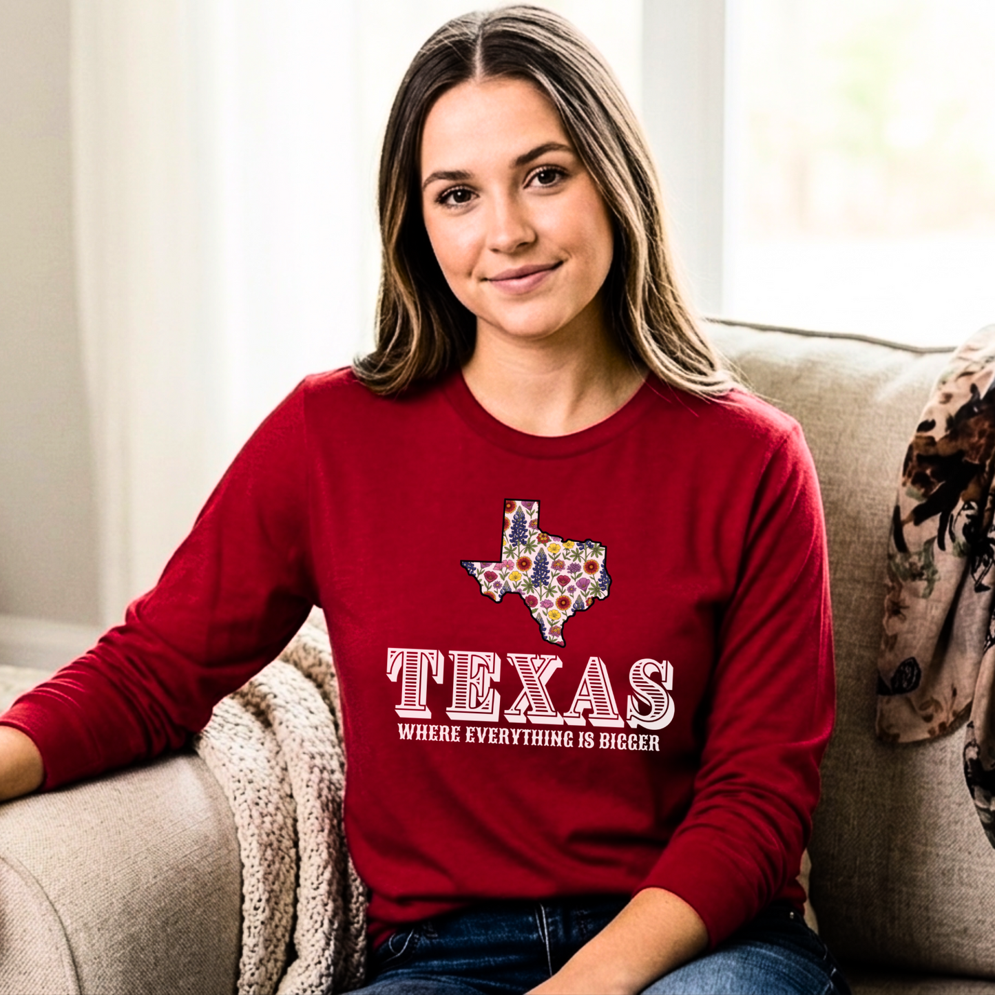 Woman wearing a red sweatshirt with a Texas design sitting on a couch.
