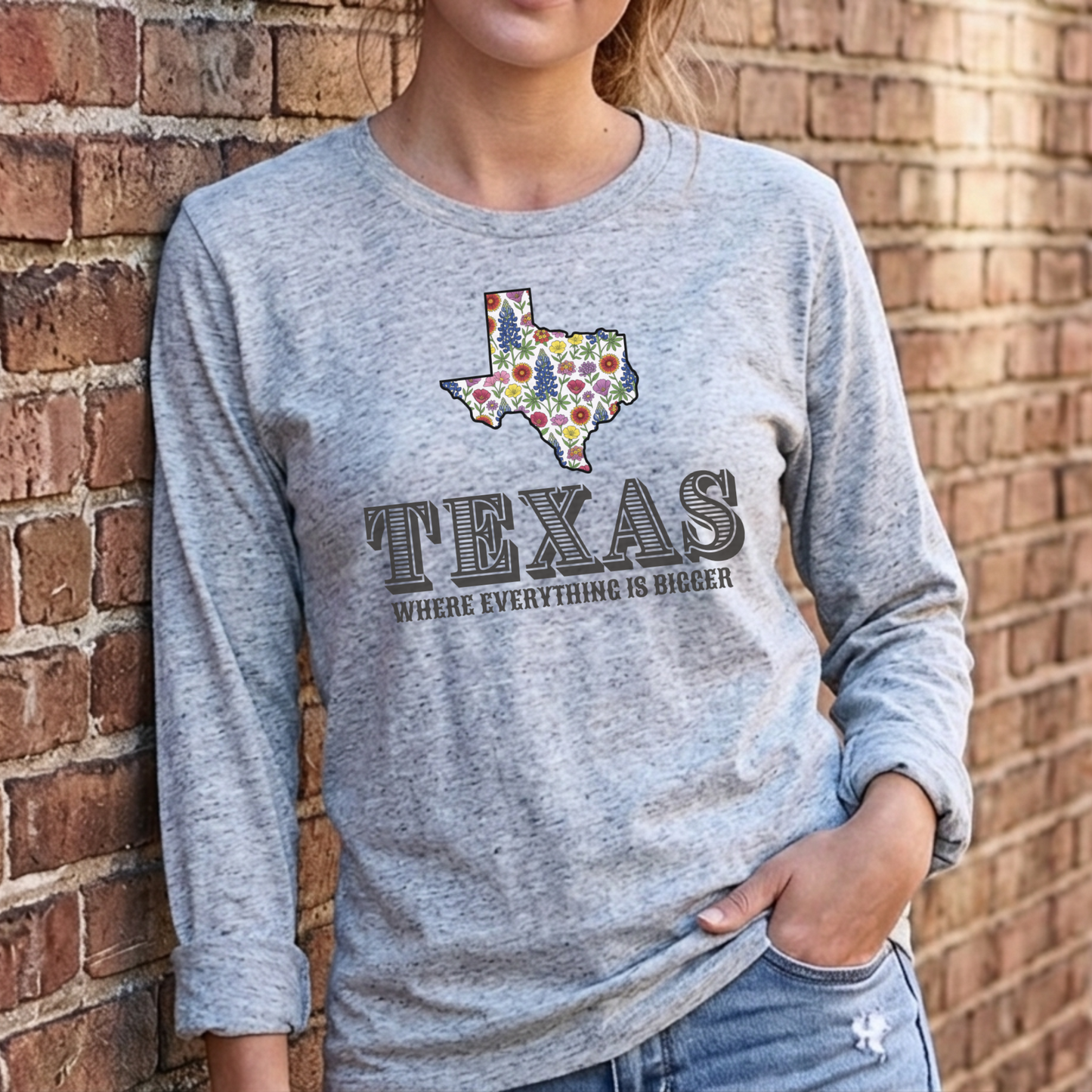 Person wearing a gray long-sleeve shirt with a Texas design against a brick wall.