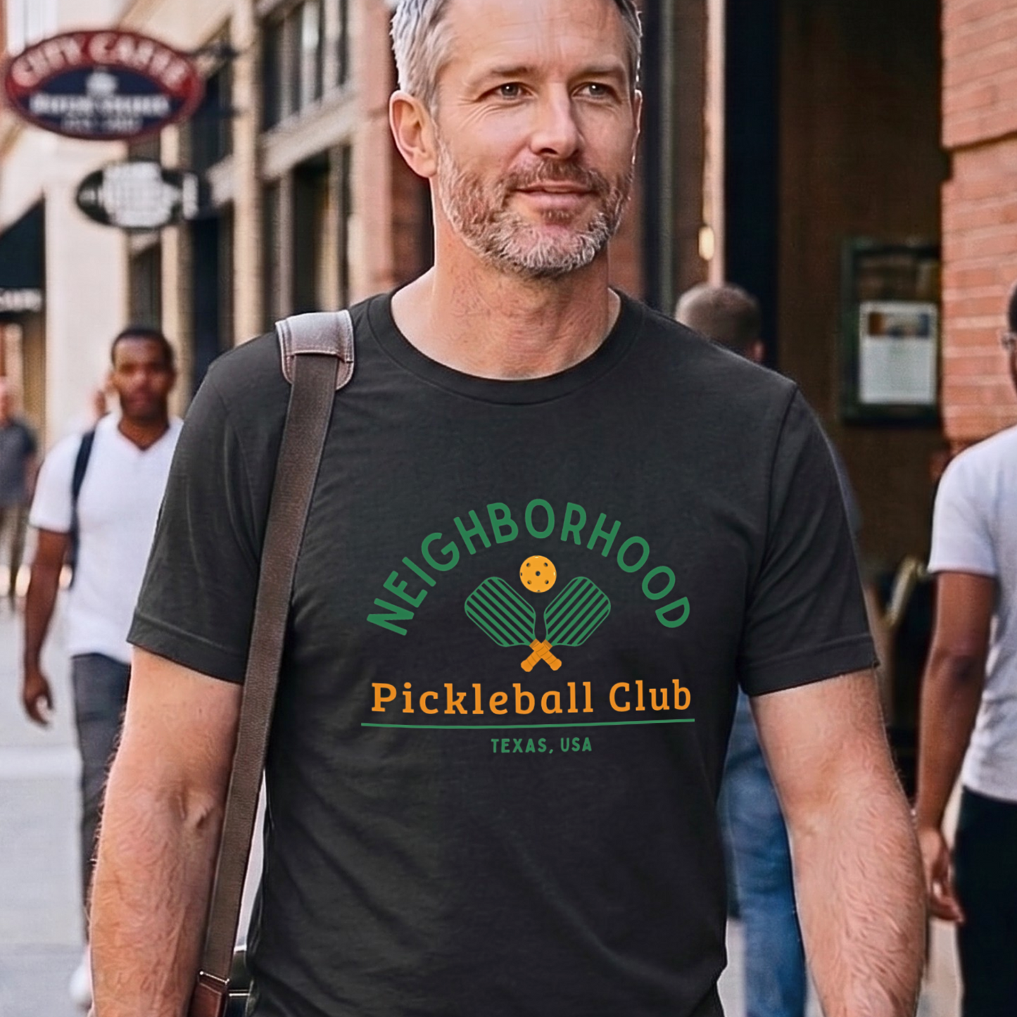 Man wearing a 'Neighborhood Pickleball Club Texas, USA' t-shirt on a city street.