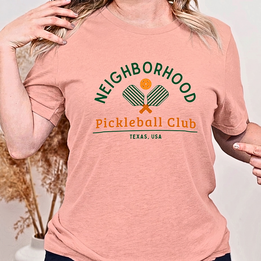 Person wearing a peach t-shirt with 'Neighborhood Pickleball Club' design.