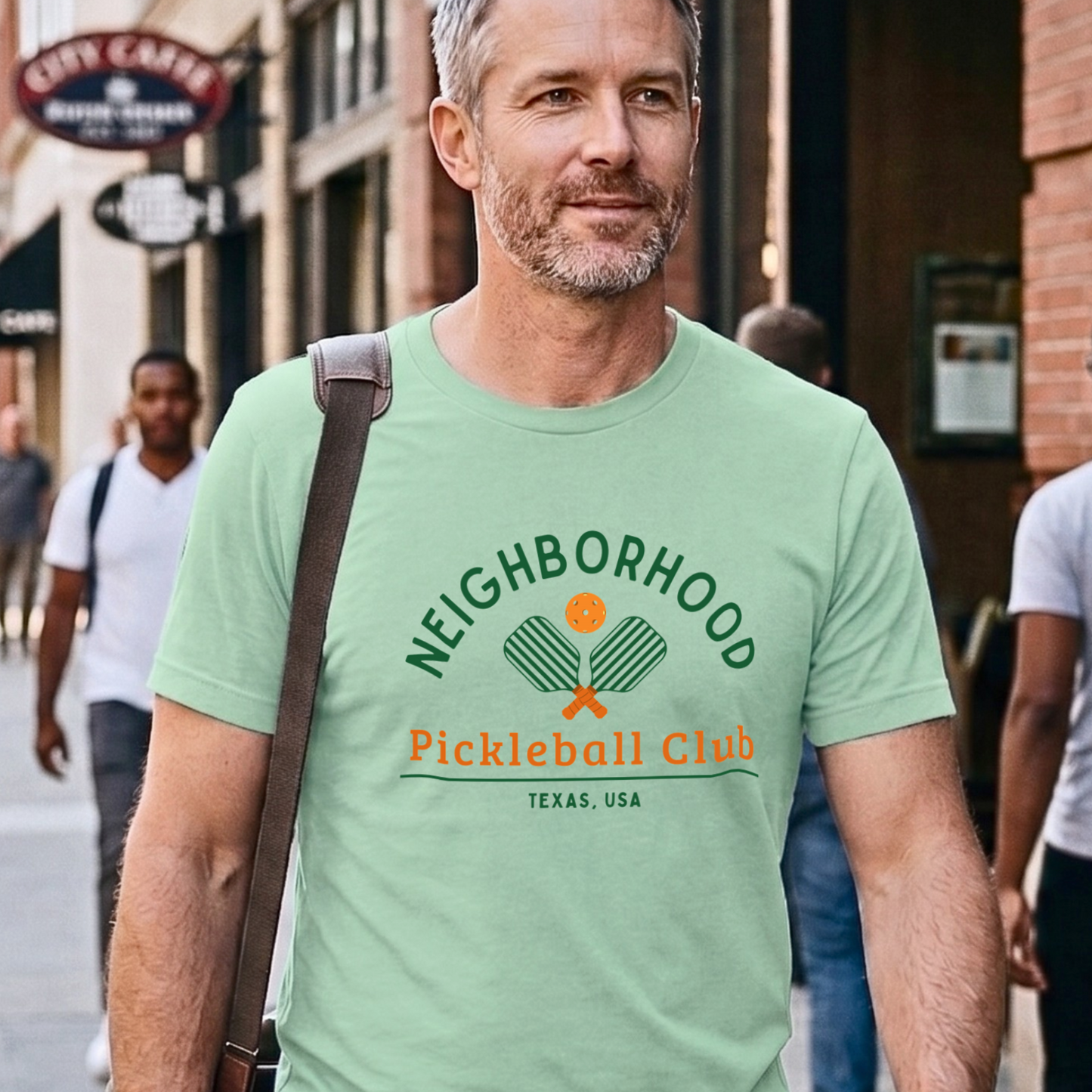 Man wearing a green t-shirt with 'Neighborhood Pickleball Club Texas, USA' text on a city street.